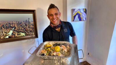 Celebrity chef Christopher Nirschel holding a gourmet catering tray of truffle risotto with fresh farm vegetables.