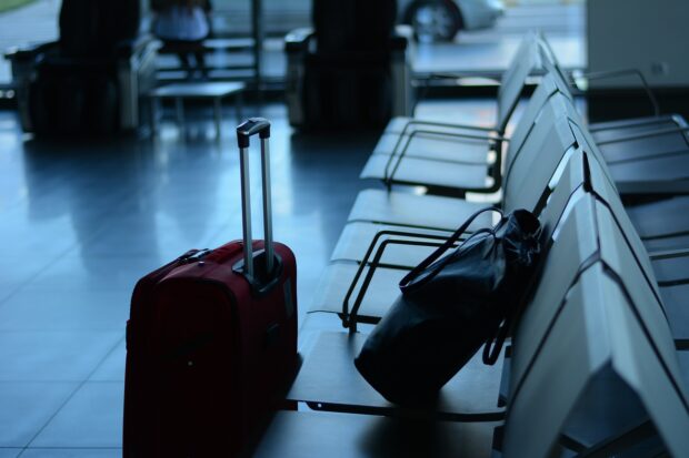 A Red Suitcase And A Backpack On A Bench In An Airport.