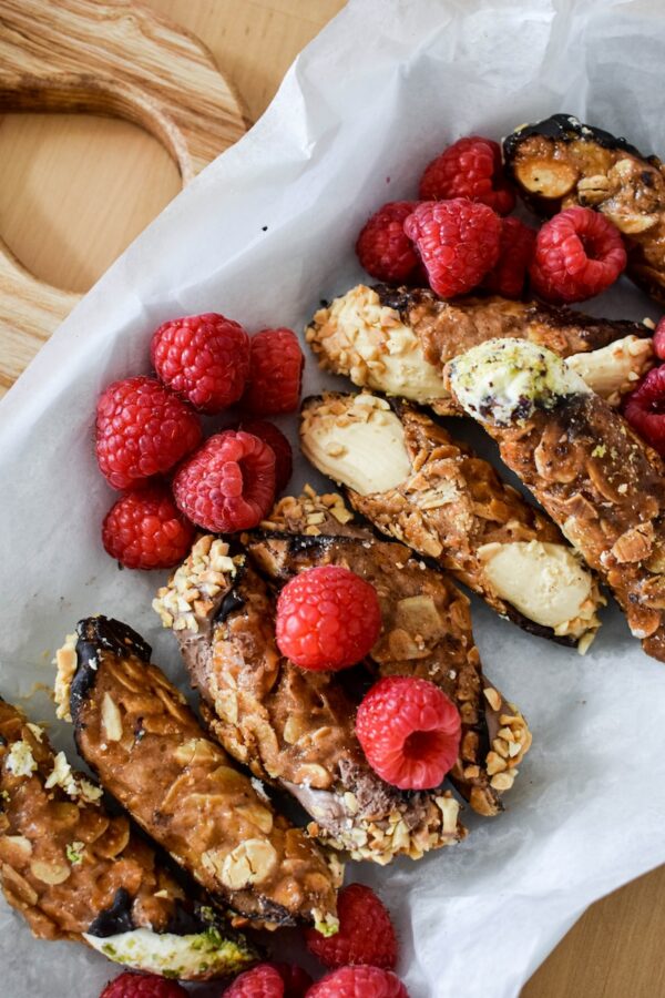 A Festive Plate Of Cannolis Adorned With Raspberries And Almonds, Perfect For The Feast Of The Seven Fishes Or Christmas Eve Dinner.