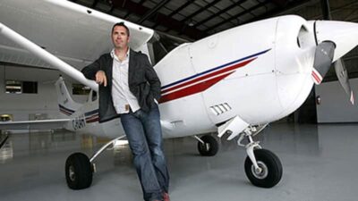 Ed Robertson From The Band, The Barenaked Ladies, Standing Next To A Small Airplane In A Hangar.