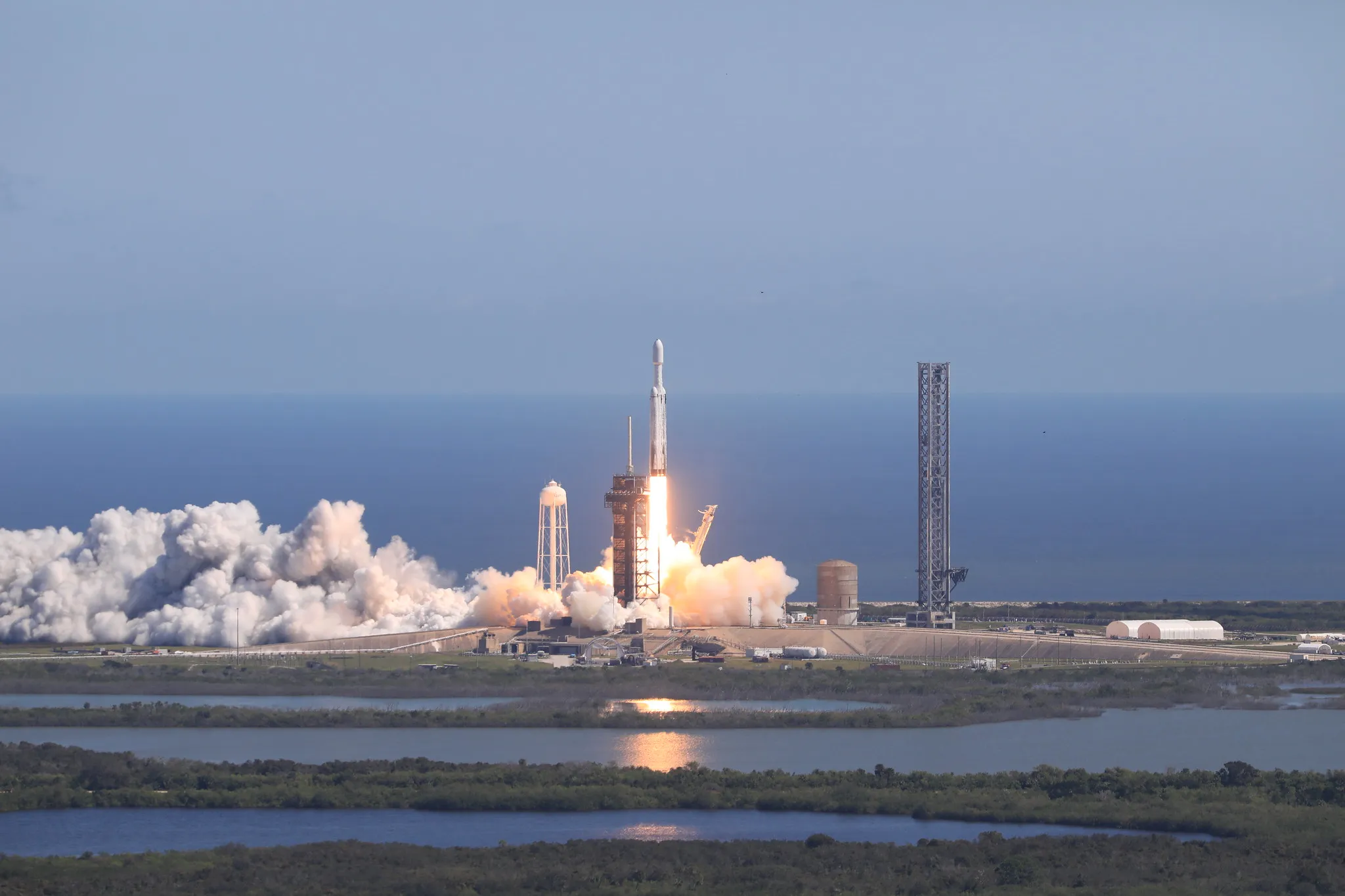 A Rocket Launching From A Coastal Pad, Smoke Billowing Against The Clear Sky, Embarks On A Mission To Explore Jupiter'S Moon, One Of The Ocean Worlds Where Alien Life Might Dwell.