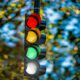 Four-Color Traffic Lights - A traffic light shows red, yellow, green, and white lights illuminated against a blurred background of leafy trees.