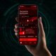 Iphone Red Screen Trick - A Hand Holding A Smartphone Displaying A Digital Audiobook Titled &Quot;The Hunt For Red October.&Quot; The Iphone Screen, With A Subtle Red Tint, Shows The Book Cover, A Play Button, And Additional Details Against A Dark Background.