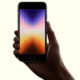 iPhone SE: A hand holding a smartphone with a colorful gradient screen displaying vertical bars, possibly the upcoming iPhone SE 4 aiming to capture the mid-range smartphone market.