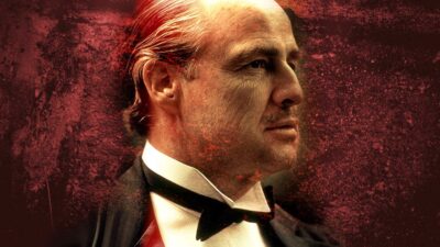 Marlon Brando from The Godfather - An older man, reminiscent of a character from The Godfather, wearing a black bow tie and suit, looks to the left against a dark, textured red background. His gaze suggests an air of spontaneity as if he's about to deliver lines without cue cards.