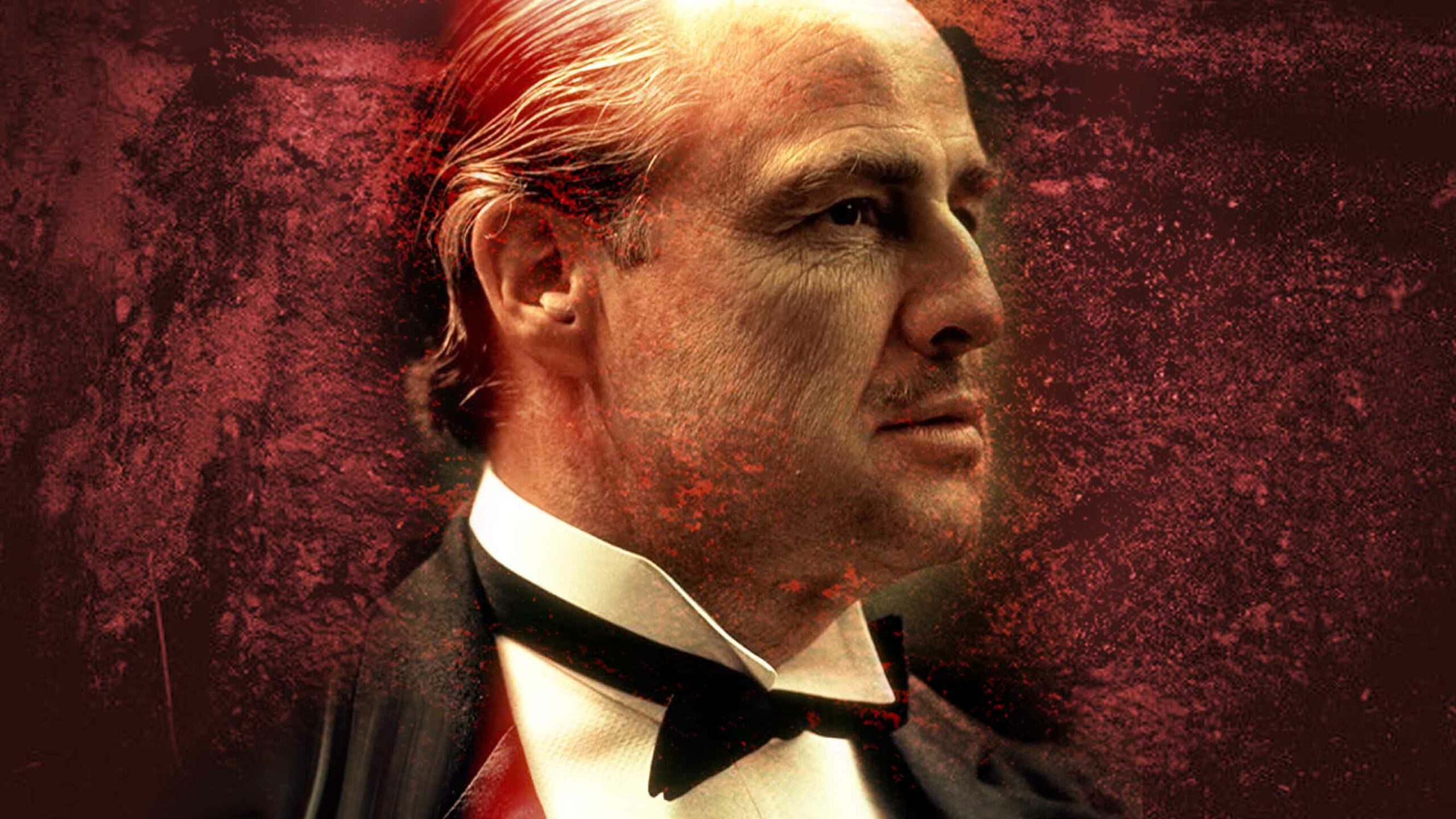 Marlon Brando From The Godfather - An Older Man, Reminiscent Of A Character From The Godfather, Wearing A Black Bow Tie And Suit, Looks To The Left Against A Dark, Textured Red Background. His Gaze Suggests An Air Of Spontaneity As If He'S About To Deliver Lines Without Cue Cards.