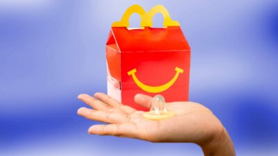 A hand holding a condom with McDonald'sHappy Meal box in the background