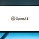 Minimalistic display of OpenAI logo on a monitor with a gradient blue background, representing modern technology.