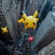 Large Pikachu balloons float above a crowded city street lined with tall buildings during the NBC parade, delighting onlookers both in person and through streaming options on Peacock.