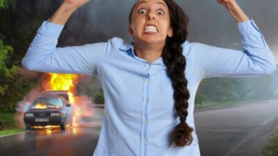 A woman stands in front of a burning car, a possible result of road rage.