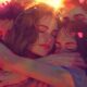 Sad Group Hug - A group of people sharing a close embrace in a warm, sunlit, artistic scene with soft pink highlights, reminiscent of the comforting moments often found in non-religious funeral gatherings.
