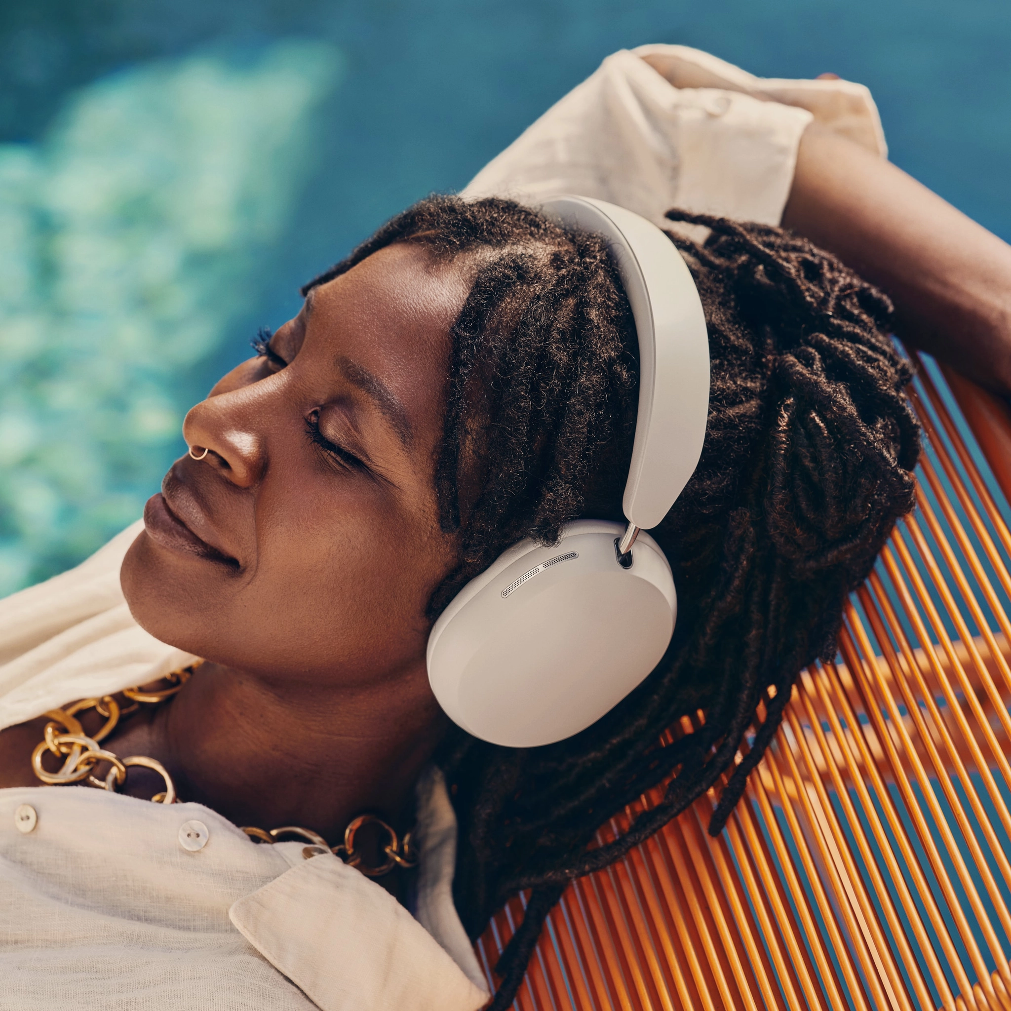 Sonos Ace Headphones - A Person With Dreadlocks Wearing Sonos Ace Headphones Relaxes On An Orange Striped Lounge Chair Near A Pool.